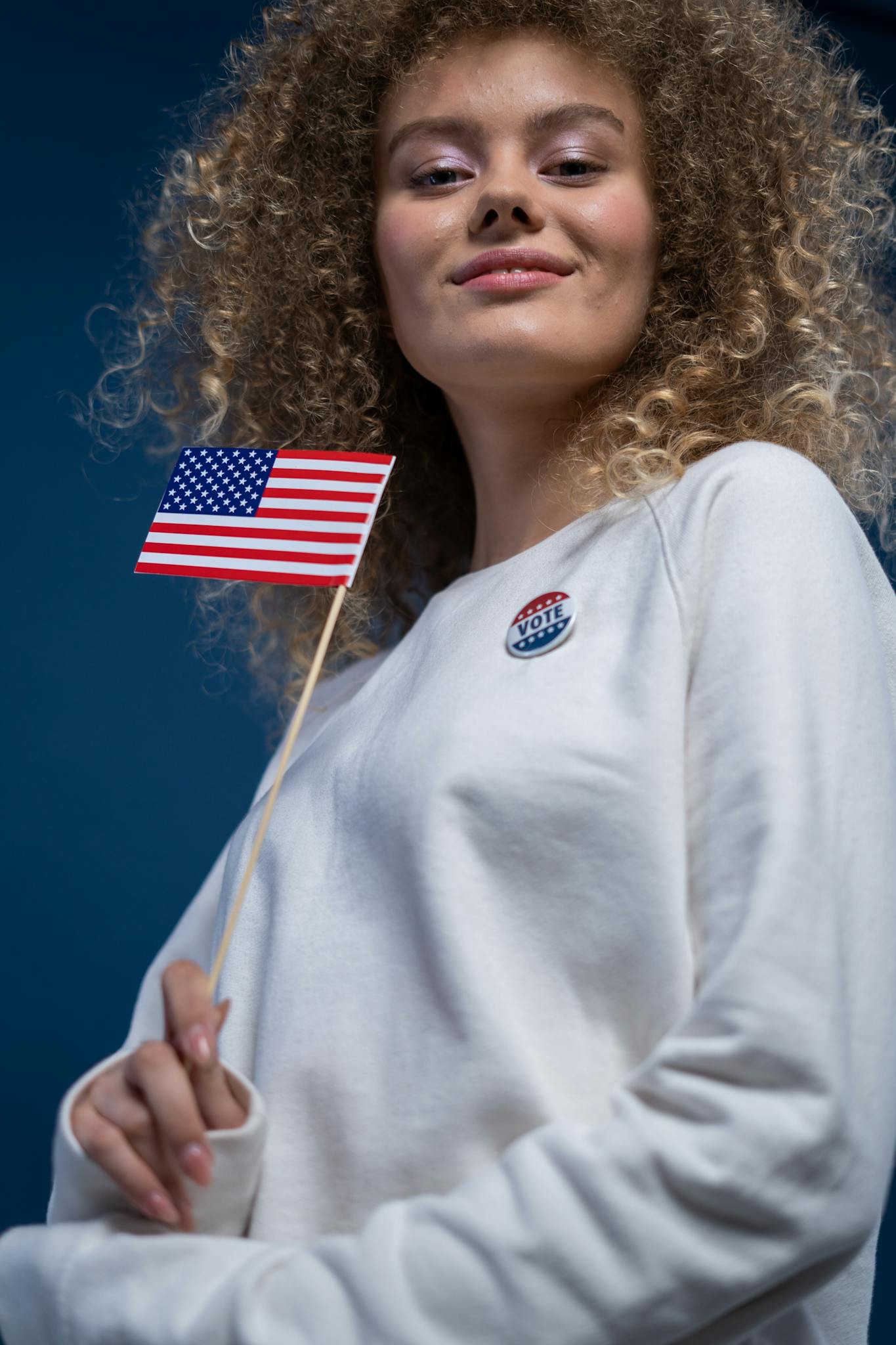 Confident young woman holding an American flag and wearing a voting button, promoting civic engagement.